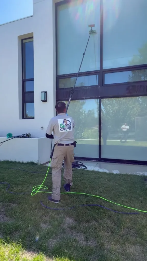 Dr. Carpet technician rinsing large glass windows with pure water