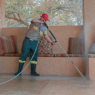 Technician pressure washing a patio floor and built-in bench next to outdoor cushions