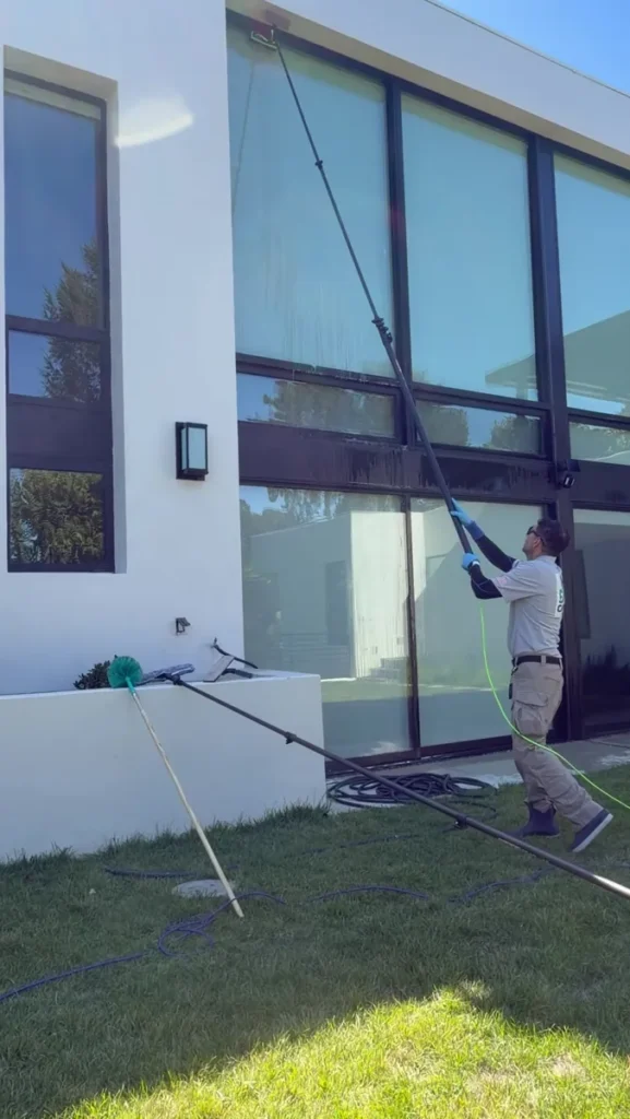 Dr. Carpet technician cleaning two-story windows of a modern East Bay home with a water-fed pole