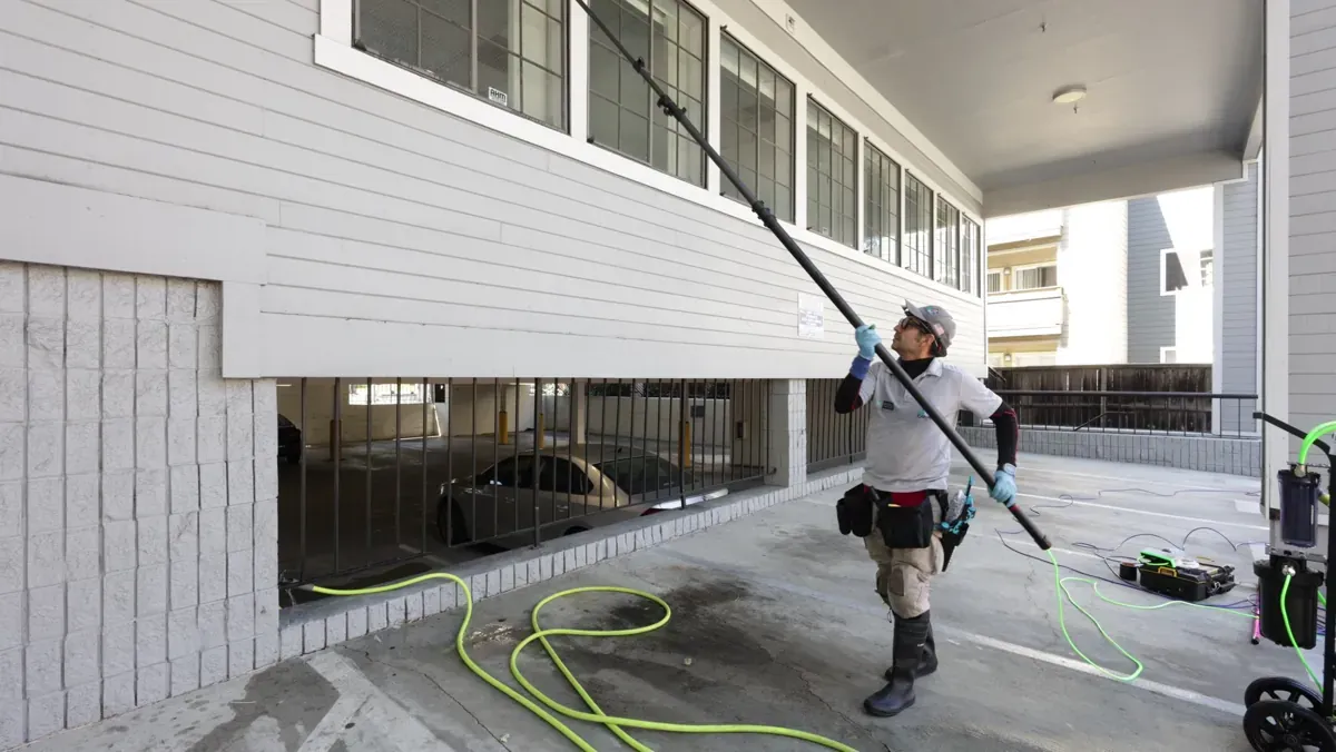 Dr. Carpet technician cleaning upper windows of a commercial building with a water-fed pole in the East Bay